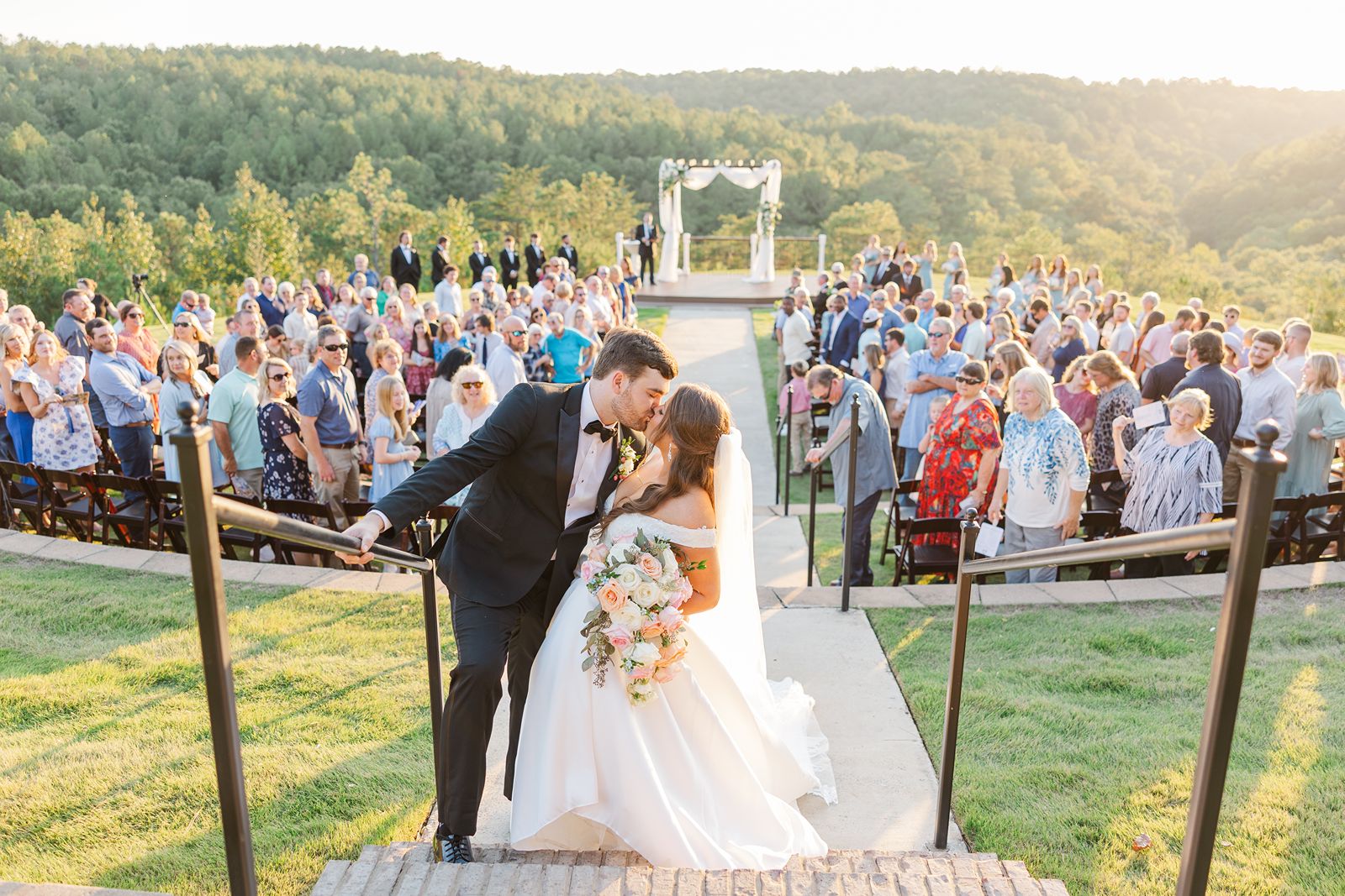 Bride and groom kissing in aisle at golden hour as guests look on at Windgate Farms in Jasper, Alabama.