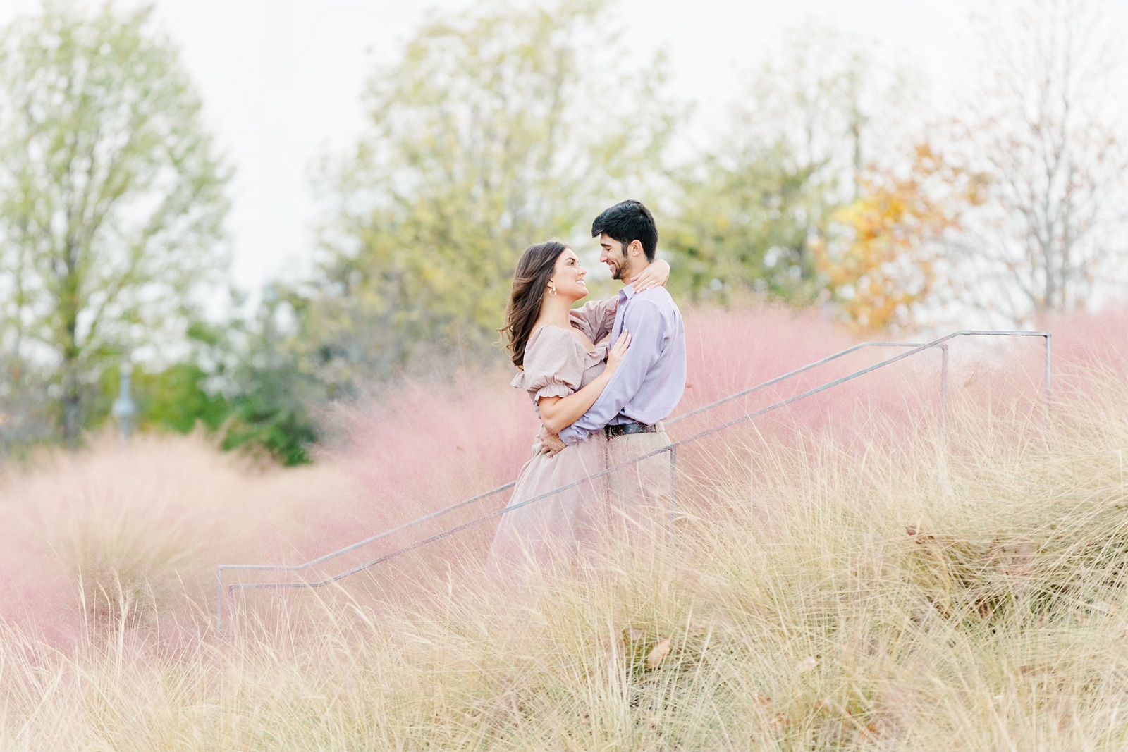 Couple embrace during engagement session surrounded by pink muhly grass at Railroad Park in Birmingham, Alabama