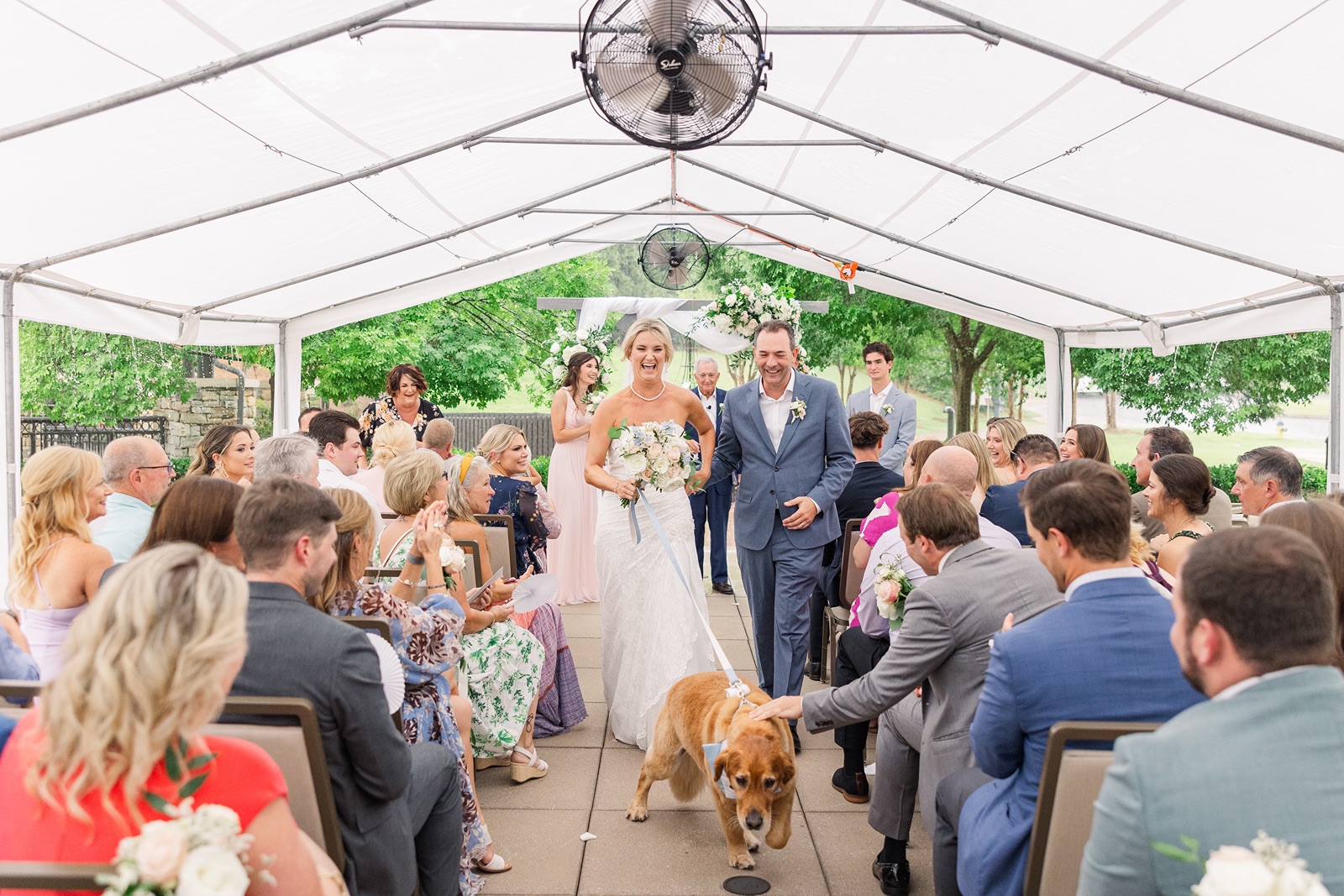 Happy couple walking up the aisle after their wedding ceremony being pulled by their Golden Retriever